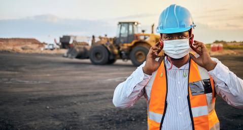 Miner with helmet and safety waistcoat in front of an excavator
