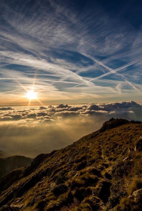 Mountain tops piercing through a cloudscape, with the sun peeking over the horizon and dramatically illuminating the clouds