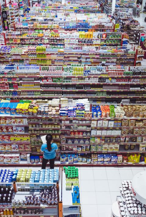 Eine Konsumentin muss zwischen Supermarkt-Regalen eine Entscheidung treffen