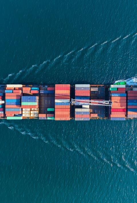 Ein Frachtschiff mit Containern auf dem offenen Meer in der Vogelperspektive von oben fotografiert