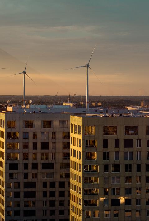 Wind turbines stand behind a city backdrop. 