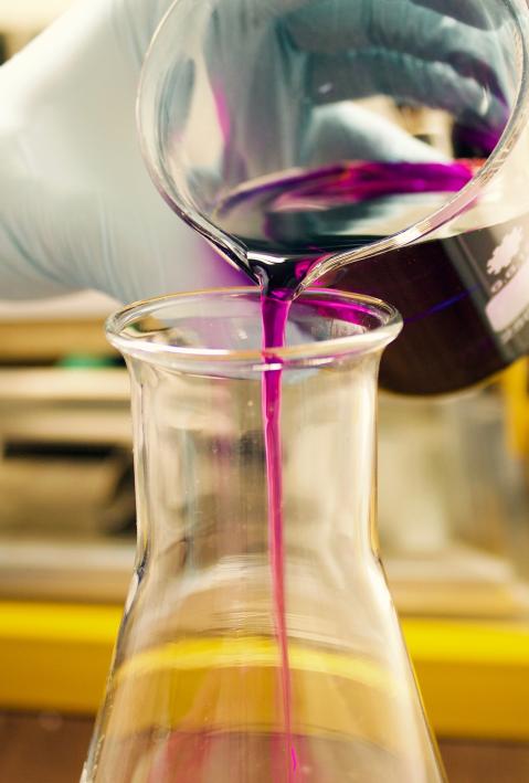 Eine Hand gießt eine lila Chemikalie in ein Reagenzglas. 