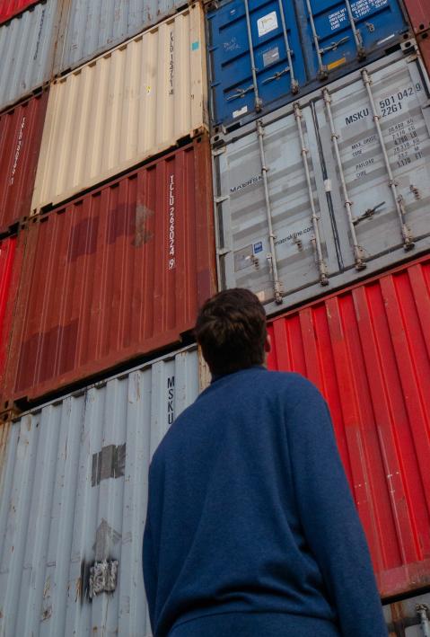 A man looks at containers stacked on top of each other. He stands with his back to the camera.