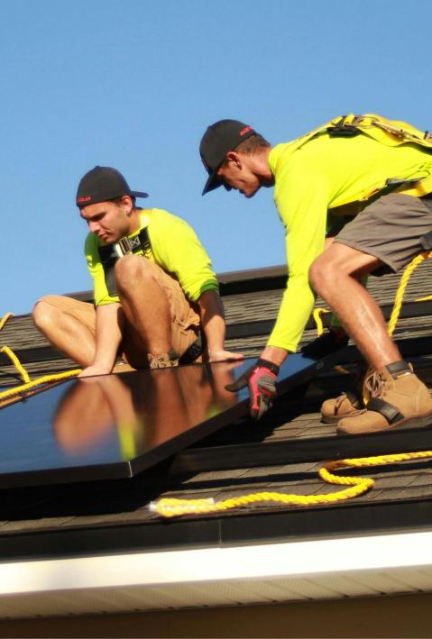 Zwei M&auml;nner arbeiten bei blauem Himmel auf einem Dach, um Photovoltaik-Platten anzubringen.