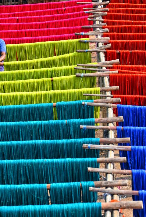 Ein Arbeiter kontrolliert farbige aufgehängte Textilfasern in Indien