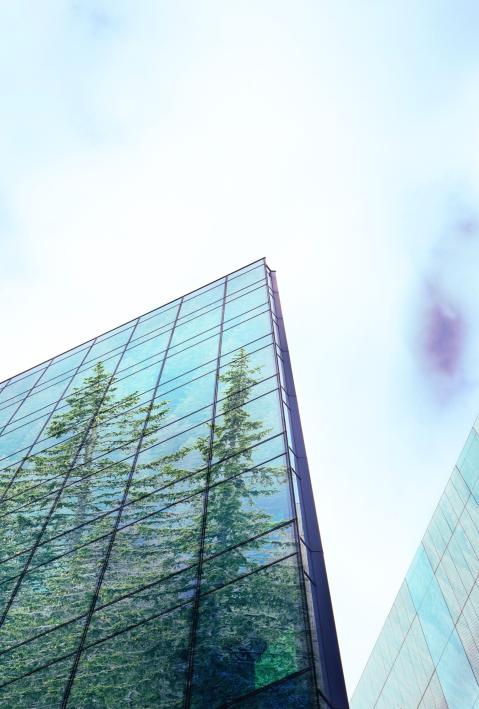 Froschperspektive auf hohe Glasgebäude, in denen sich Bäume spiegeln, blauer Himmel mit vereinzelten Wolken