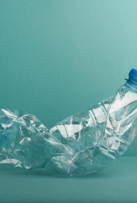 Eine leere, zerknüllte Plastikflasche vor einem blaugrünen Hintergrund