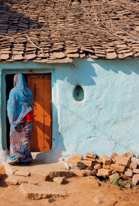 House of poor family and indian woman standing at the door of traditional style home, India.