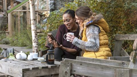Two friends using mobile device and drinking tea after harvesting in the garden, London, UK, Europe,morning.
