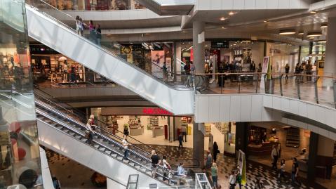 Innenansicht eines Einkaufszentrums mit Kund:innen auf Rolltreppen