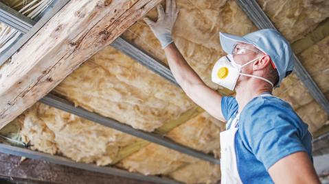 Ein Handwerker mit Schutzausrüstung kontrolliert die Wärmedämmung eines Dachstuhls