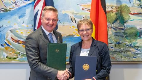 Australian Energy Minister Chris Bowen and German State Secretary Anja Hajduk shake hands while holding the signed agreement