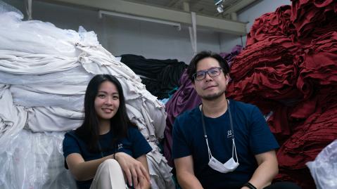 Asian-looking woman and man sitting in front of large piles of white and red textiles