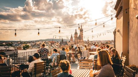 Personen genießen die Sonne und Drinks auf einer Dachterrasse in Krakau, Polen.