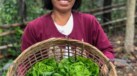 A female farmer from Thailand with a basket full of fresh greens smiling into the camera