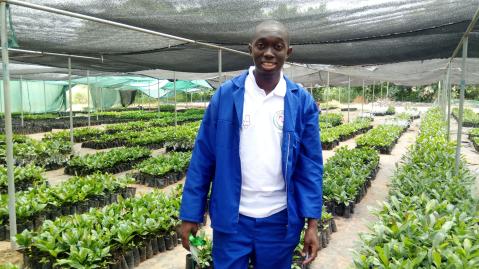 Mwala Mooto posing in from of hybrid cashew tree seedlings in a greenhouse