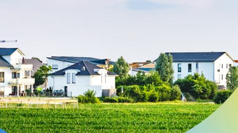 Eine Reihe von weißen Häusern mit grauen Dächern hinter einer Grünfläche mit Baukränen im Hintergrund