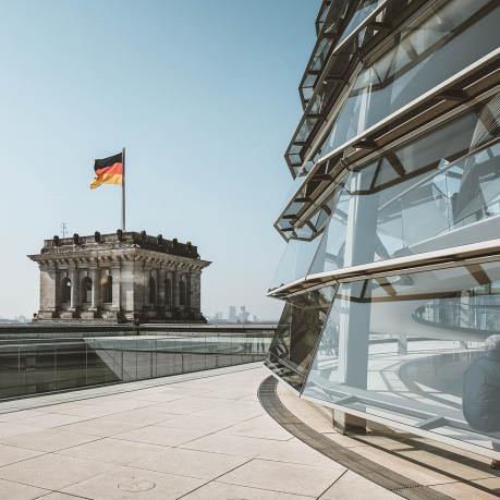 Die Kuppel des Bundestags ist abgeschnitten auf der rechten Seite des Bildes zu erkennen. Links daneben schaut man auf einen der beiden Türme mit Deutschlandflagge