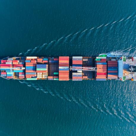 Ein Frachtschiff mit Containern auf dem offenen Meer in der Vogelperspektive von oben fotografiert
