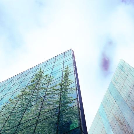 Froschperspektive auf hohe Glasgeb&auml;ude, in denen sich B&auml;ume spiegeln, blauer Himmel mit vereinzelten Wolken