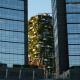 Bosco Verticale, Mailand, Italien: Zwischen zwei Hochhäusern aus Glas steht ein Gebäude im Licht, das komplett mit Pflanzen bestückt ist.