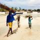 Ein Mann und zwei Kinder tragen Holz am Strand von Mosambik. 