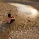 Ein Kind sitzt auf ausgetrockneter, zerrissener Erde und schaut auf eine schrumpfende Wasserlache.